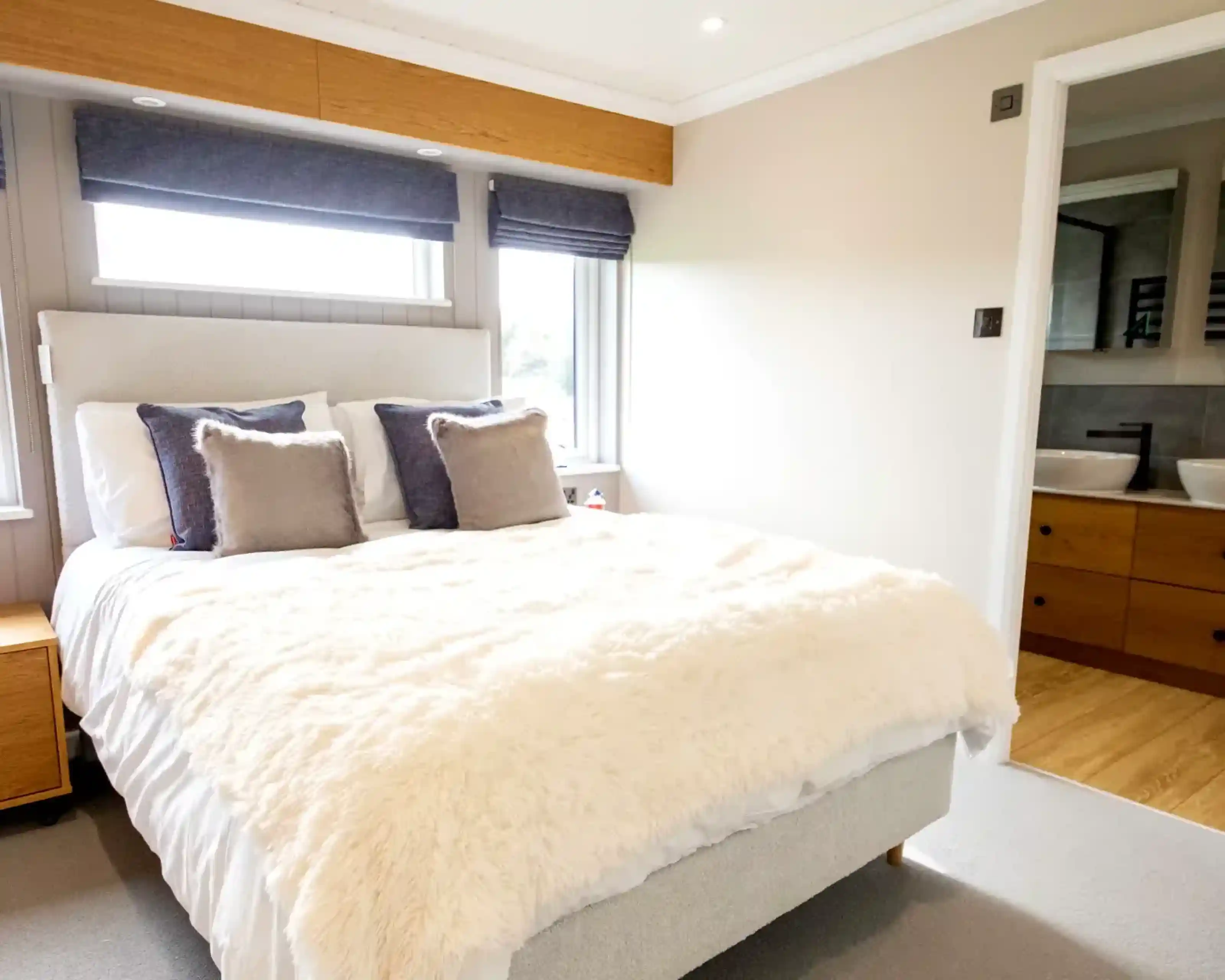 A large double bedroom featuring a plush white duvet, grey headboard, and a glimpse of a modern bathroom with double sinks.