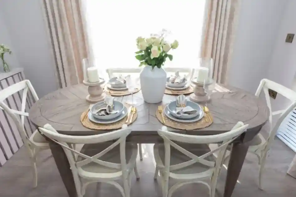 A dining table set for six with a vase of white roses and candlelight.