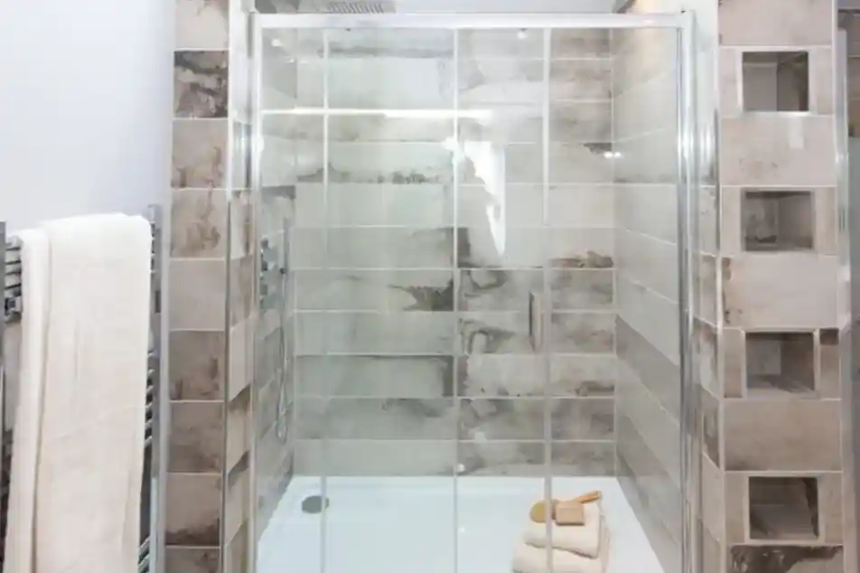 A modern shower enclosure with glass doors, tiled walls, a white shower base, and a towel rack with white towels.