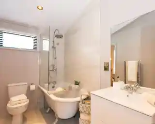 A modern bathroom features a freestanding clawfoot tub with a glass shower screen, a toilet with stacked towels, and a white vanity with a sink and mirror.