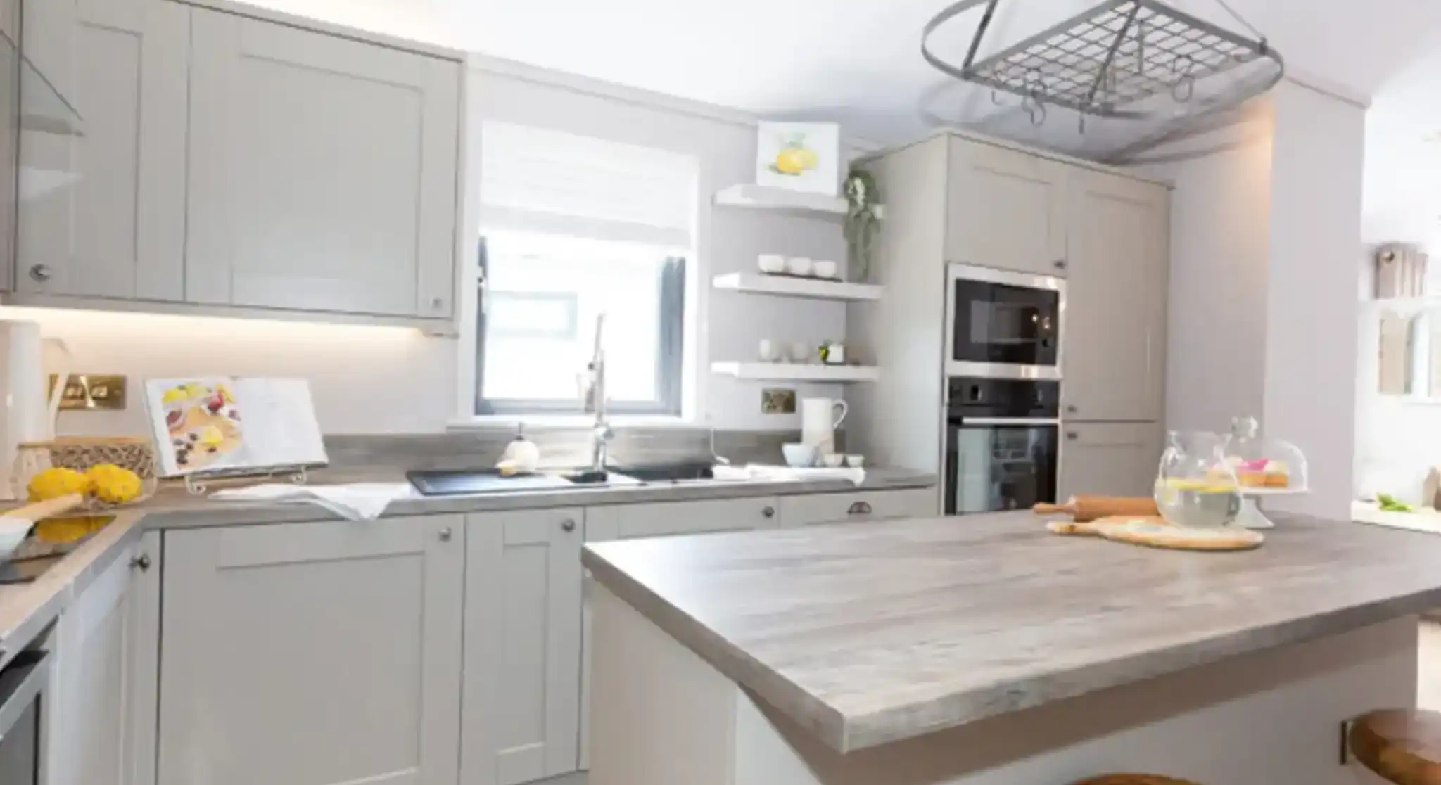 Modern grey kitchen with a central island, stainless steel appliances, and a hanging pot rack.