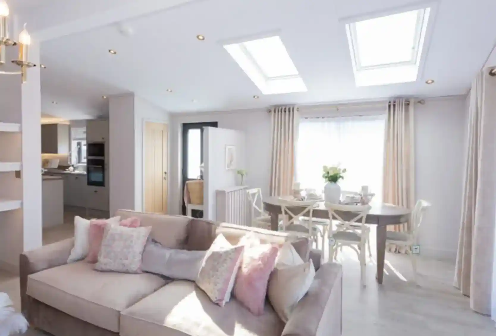 A spacious living and dining area with a plush sofa, a dining table set for a meal, and skylights illuminating the room.