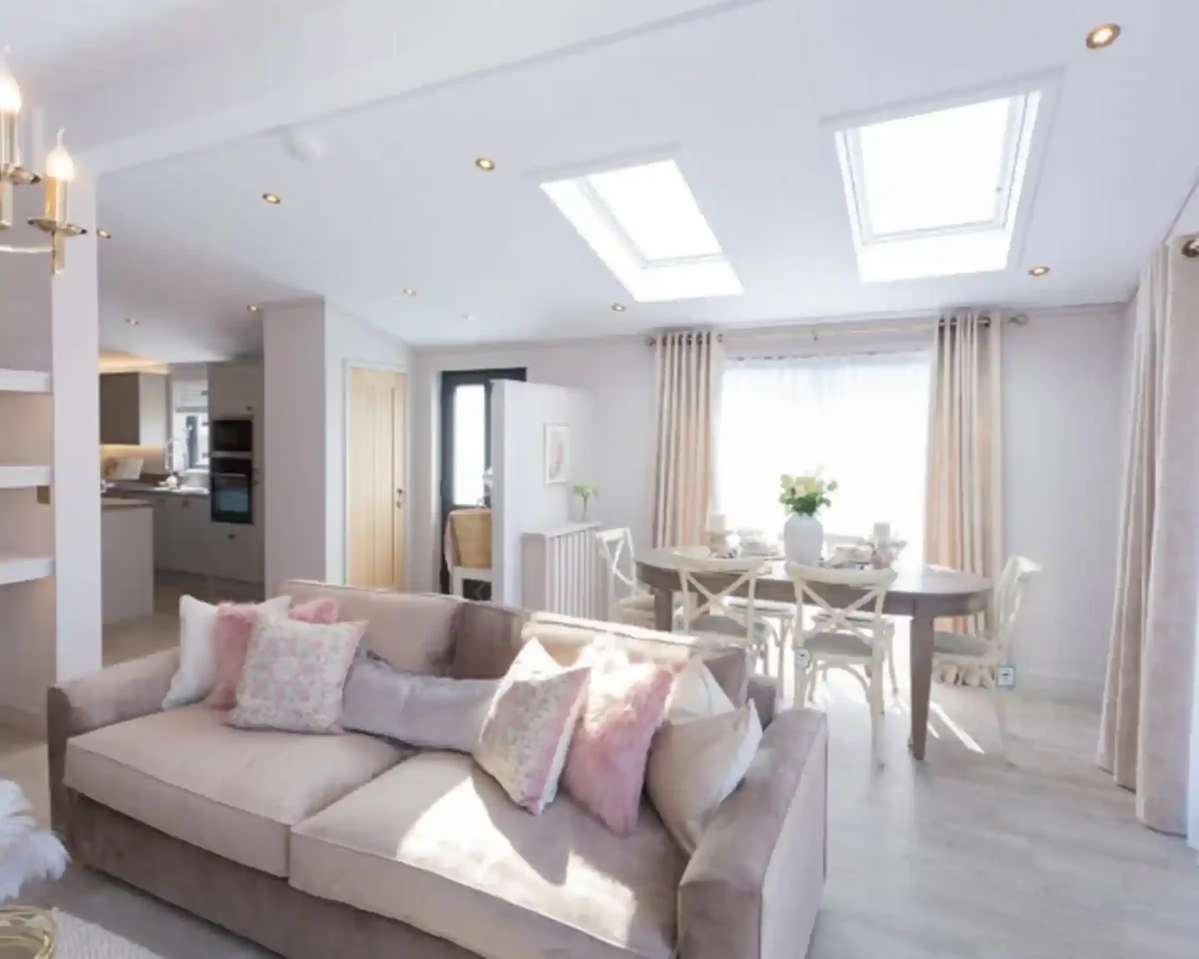 A spacious living and dining area with a plush sofa, a dining table set for a meal, and skylights illuminating the room.