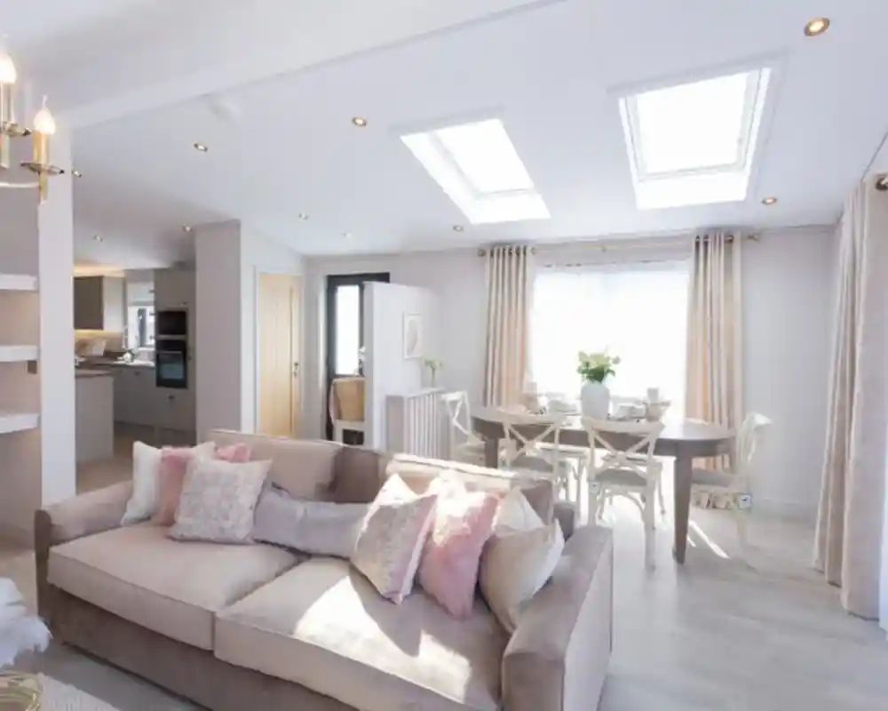 A spacious living and dining area with a plush sofa, a dining table set for a meal, and skylights illuminating the room.