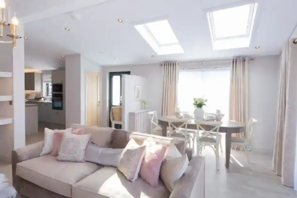 A spacious living and dining area with a plush sofa, a dining table set for a meal, and skylights illuminating the room.