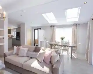 A spacious living and dining area with a plush sofa, a dining table set for a meal, and skylights illuminating the room.