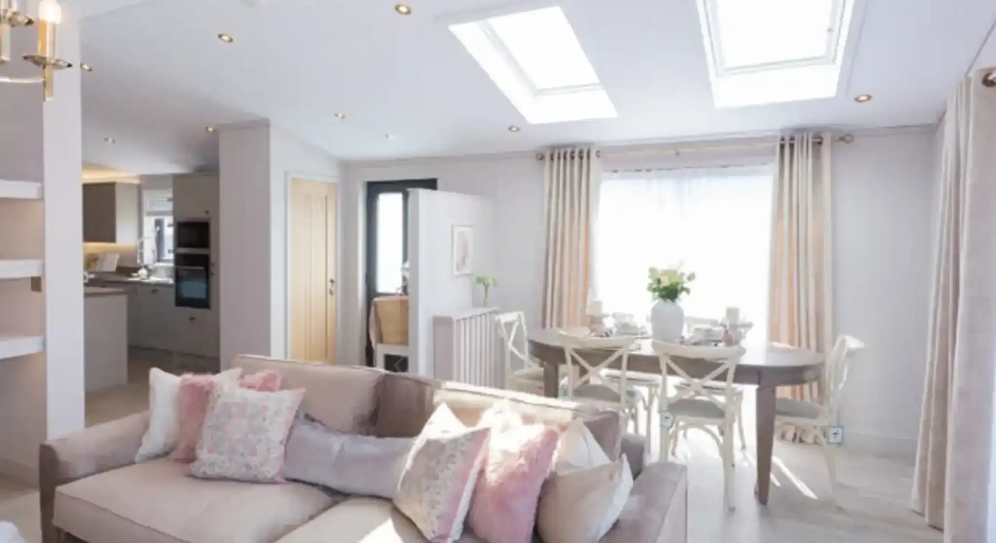 A spacious living and dining area with a plush sofa, a dining table set for a meal, and skylights illuminating the room.