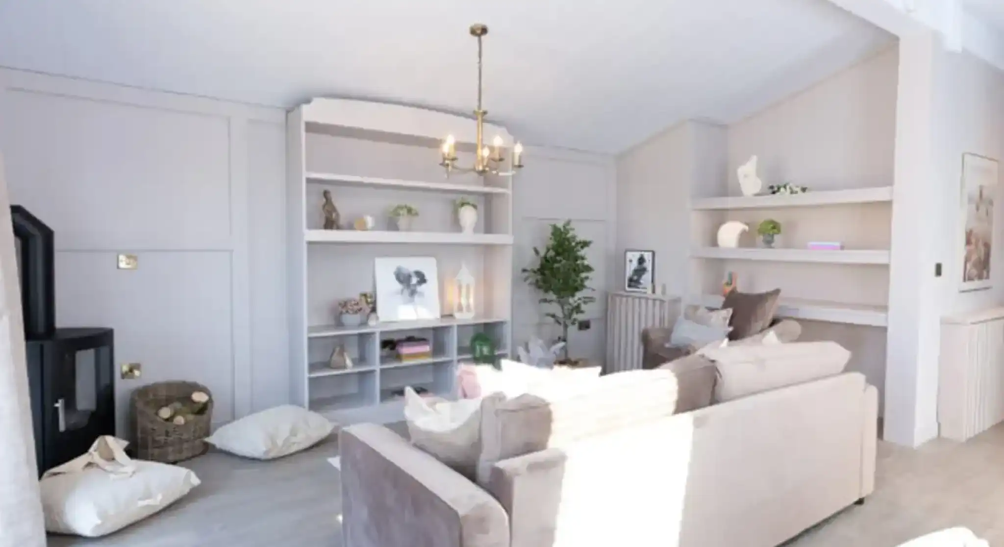 A bright, modern living room features a plush sofa, a black wood-burning stove, and built-in shelves displaying décor.