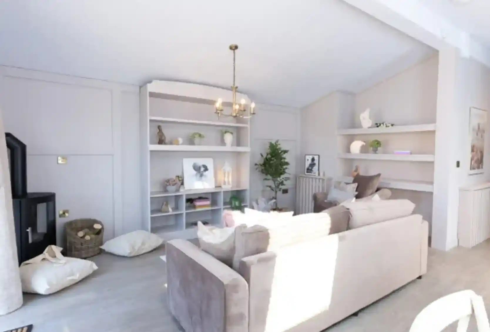 A bright, modern living room features a plush sofa, a black wood-burning stove, and built-in shelves displaying décor.