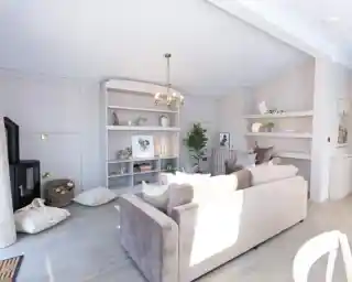 A bright, modern living room features a plush sofa, a black wood-burning stove, and built-in shelves displaying décor.