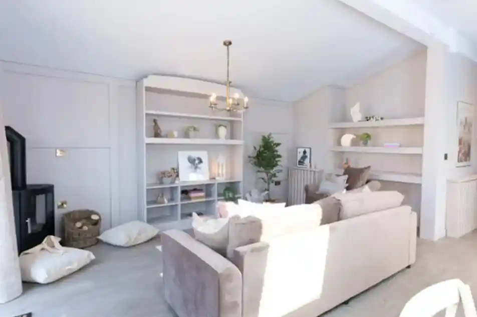 A bright, modern living room features a plush sofa, a black wood-burning stove, and built-in shelves displaying décor.