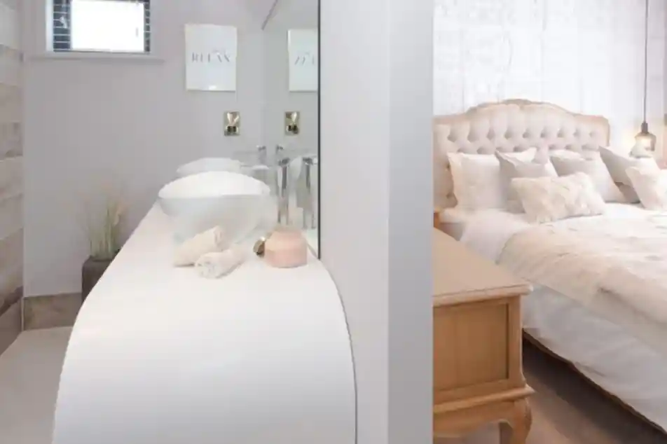 Interior view of a modern bathroom vanity area with two sinks and a glimpse of a tufted headboard bedroom.