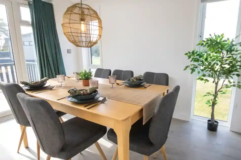 A modern dining room with a wooden table set for six, dark gray chairs, and a large wicker pendant light.