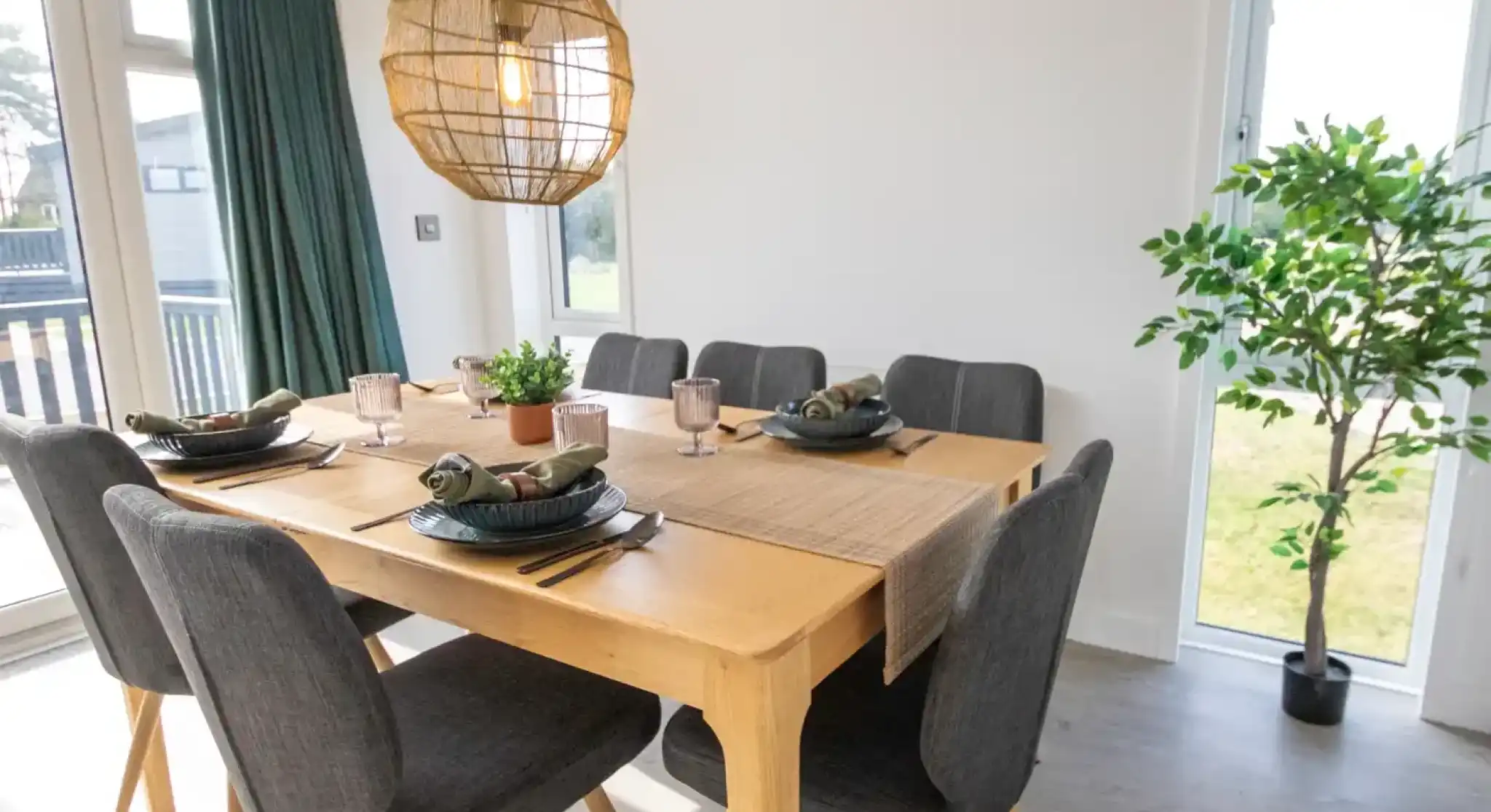 A modern dining room with a wooden table set for six, dark gray chairs, and a large wicker pendant light.