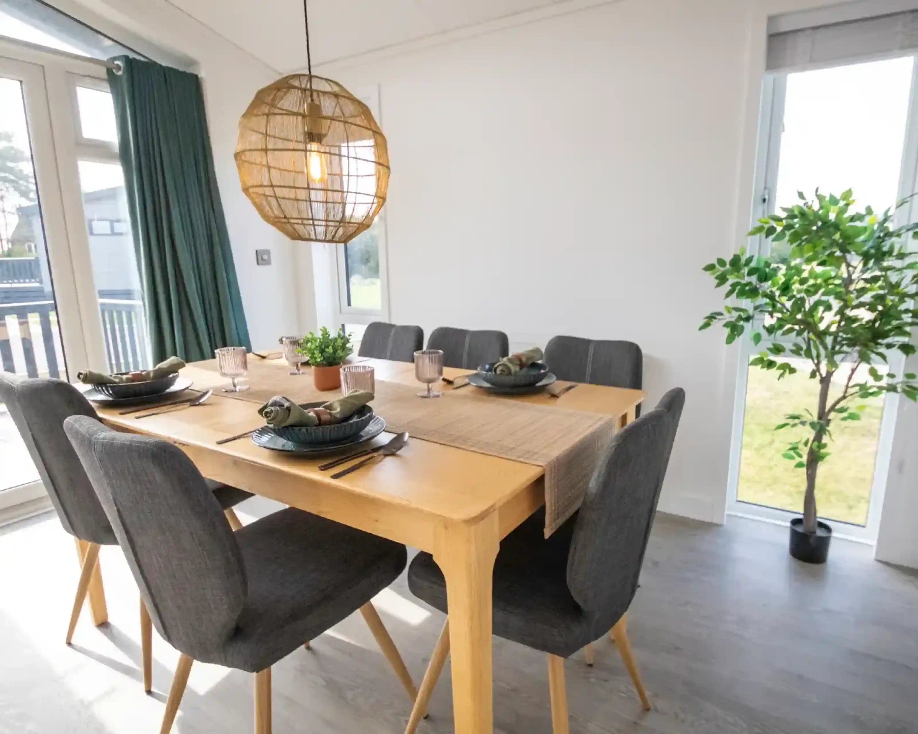 A modern dining room with a wooden table set for six, dark gray chairs, and a large wicker pendant light.