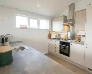 A modern kitchen featuring a stainless steel sink, oven, and range hood with white panelled walls and light wood cabinets.