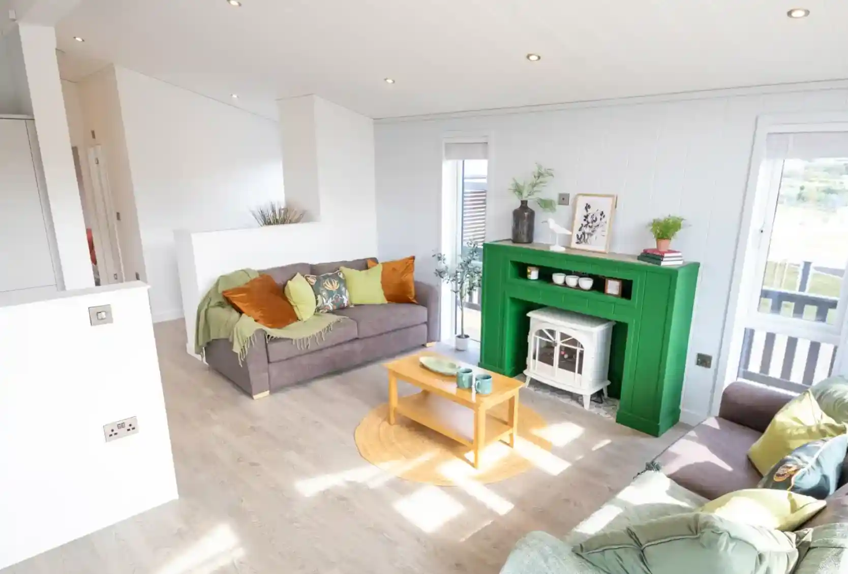 A modern living room features two sofas, a bright green fireplace with a white electric stove, and a light wood coffee table.