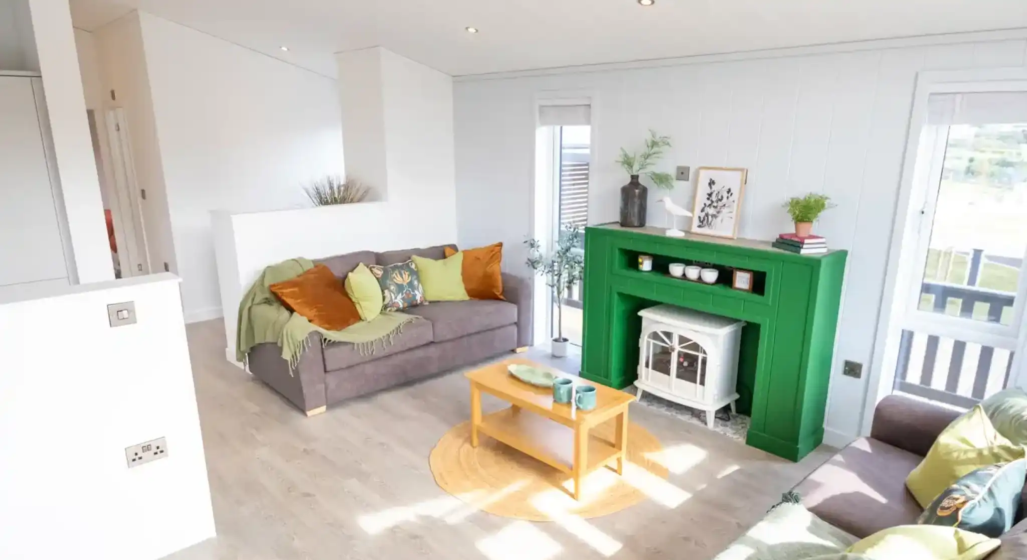 A modern living room features two sofas, a bright green fireplace with a white electric stove, and a light wood coffee table.