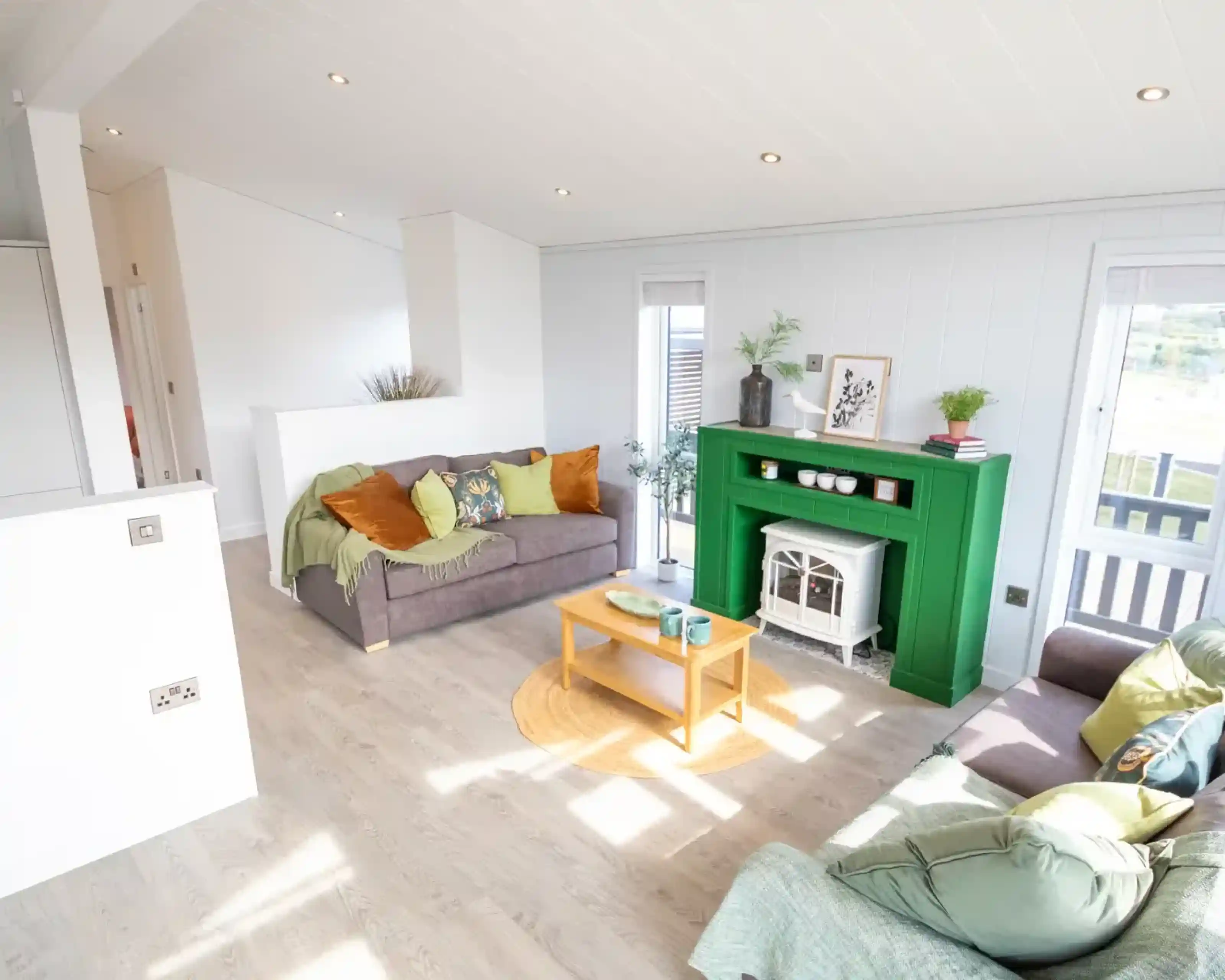 A modern living room features two sofas, a bright green fireplace with a white electric stove, and a light wood coffee table.