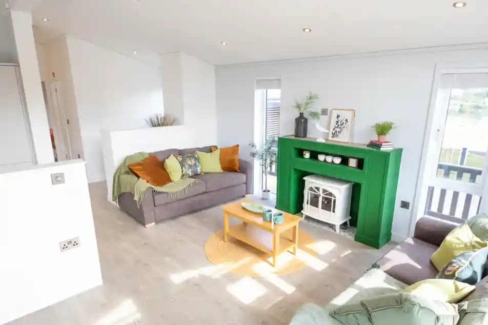 A modern living room features two sofas, a bright green fireplace with a white electric stove, and a light wood coffee table.