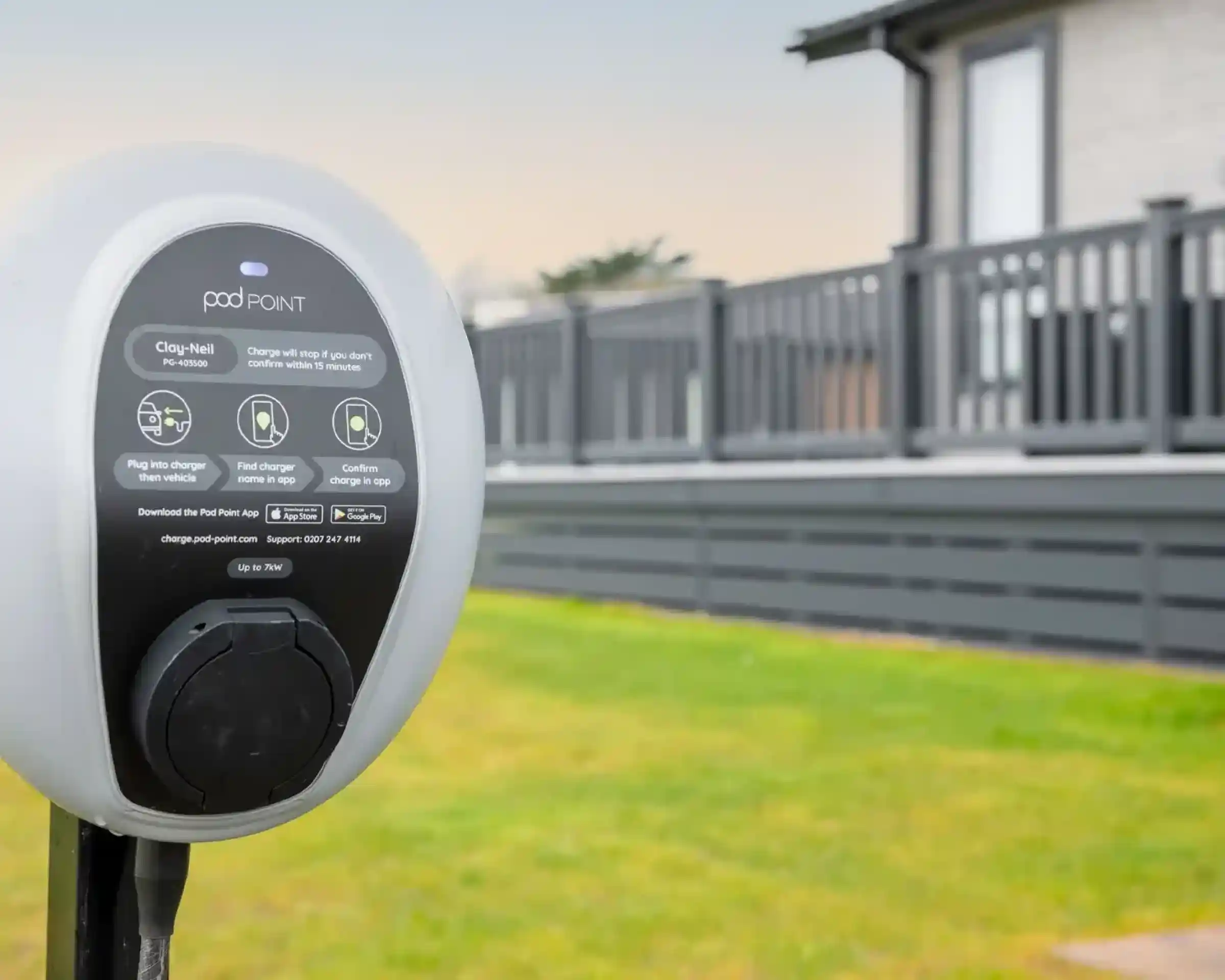 Pod Point electric car charger in front of a grey clad lodge holiday home with decking.