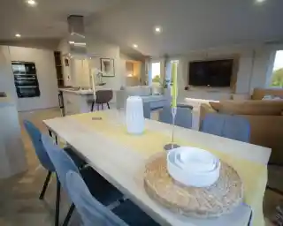 Modern open-concept living and dining area with a wooden dining table, decorative candles, and a yellow table runner.