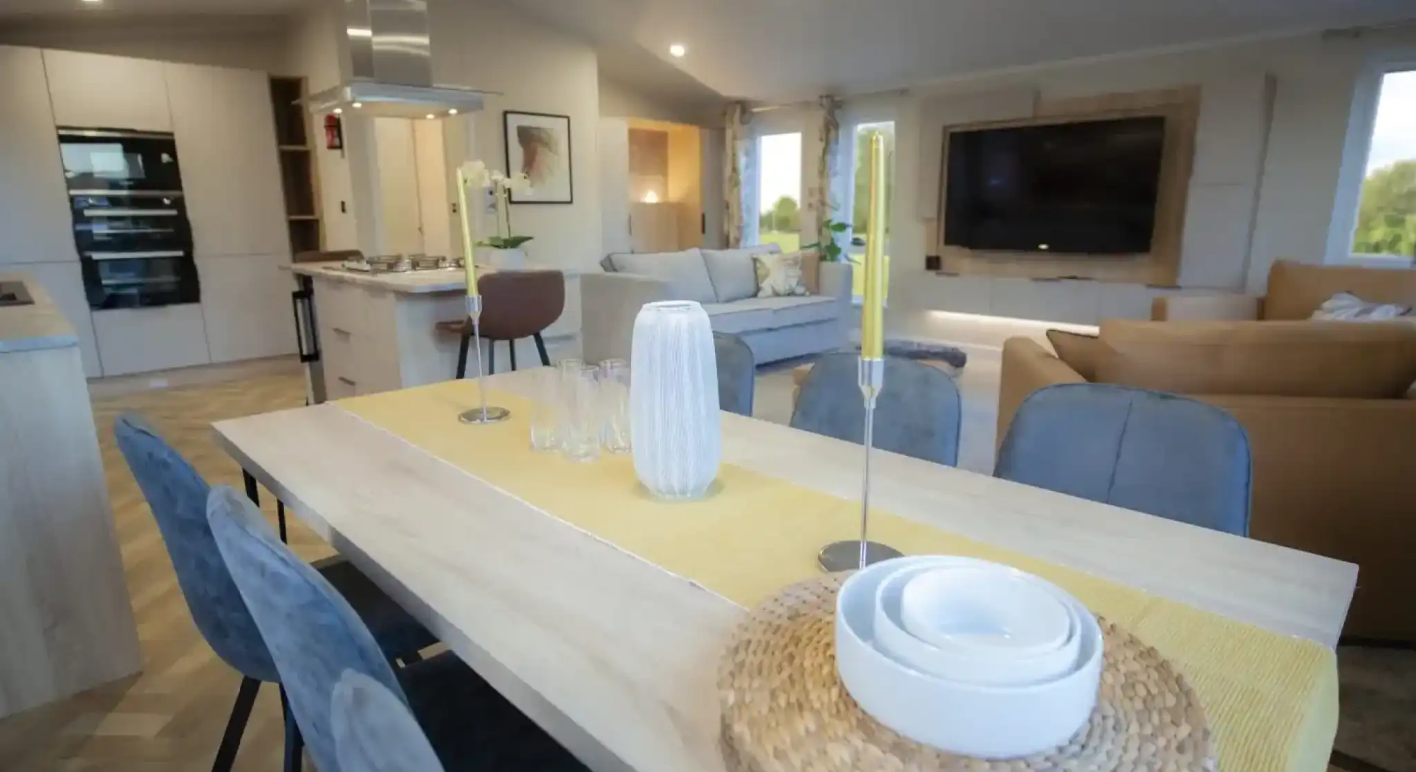 Modern open-concept living and dining area with a wooden dining table, decorative candles, and a yellow table runner.