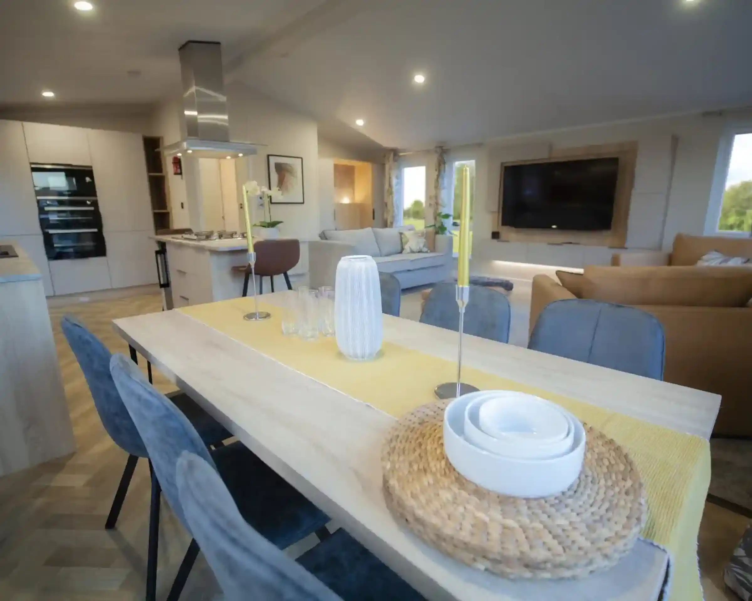 Modern open-concept living and dining area with a wooden dining table, decorative candles, and a yellow table runner.