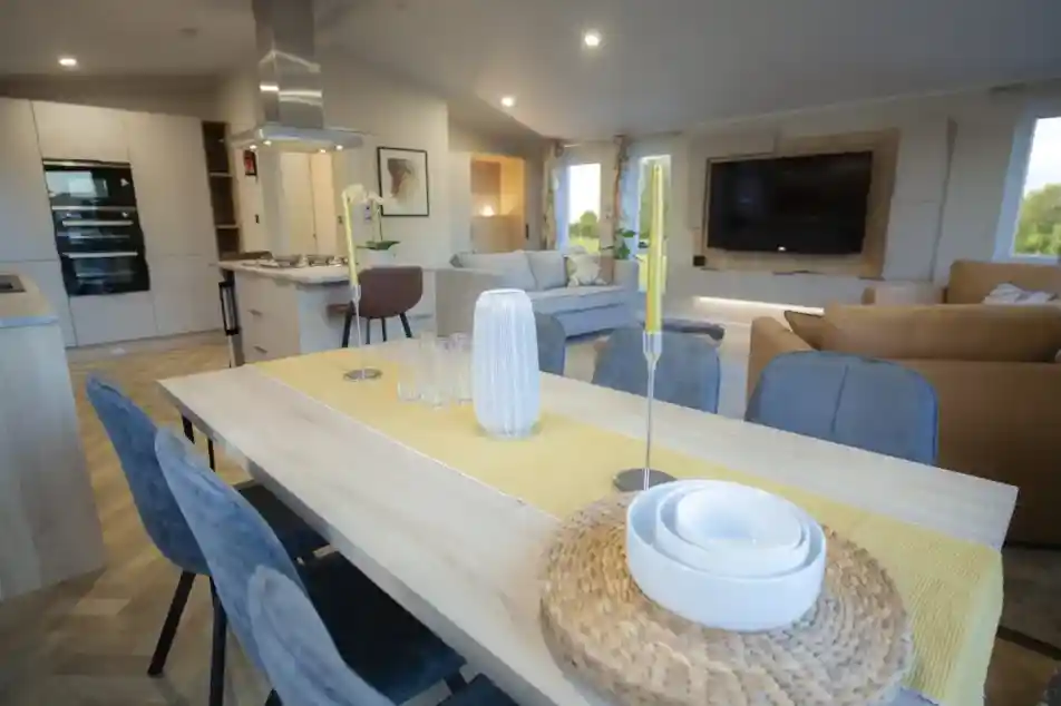 Modern open-concept living and dining area with a wooden dining table, decorative candles, and a yellow table runner.