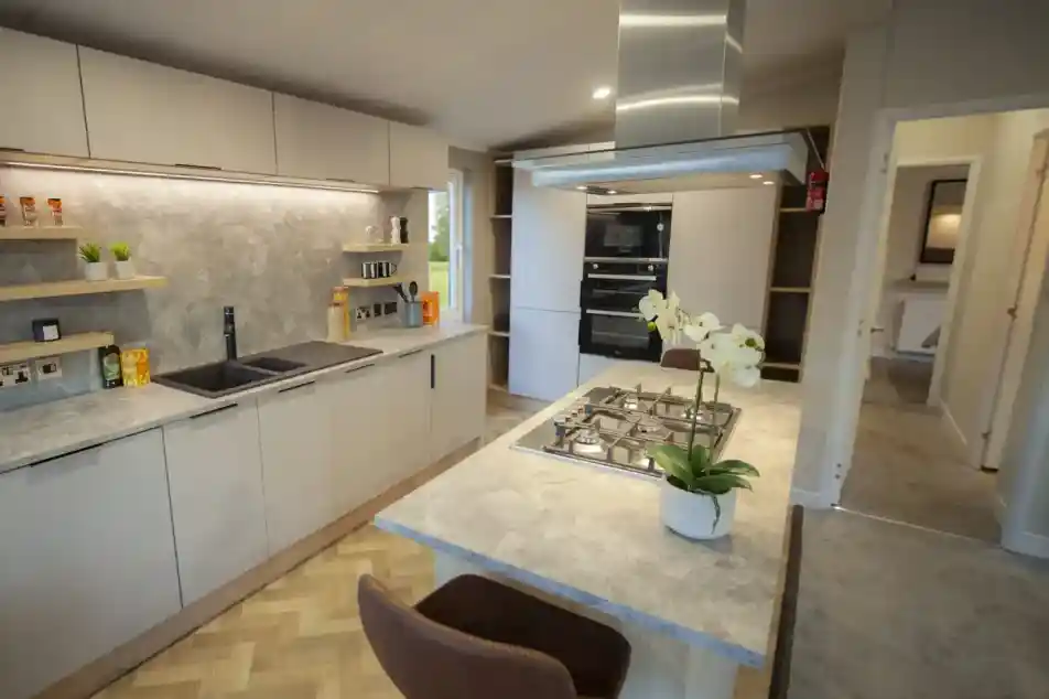 Modern kitchen featuring minimalist white cabinets, a marble countertop, and a built-in oven, illuminated by natural and recessed lighting.