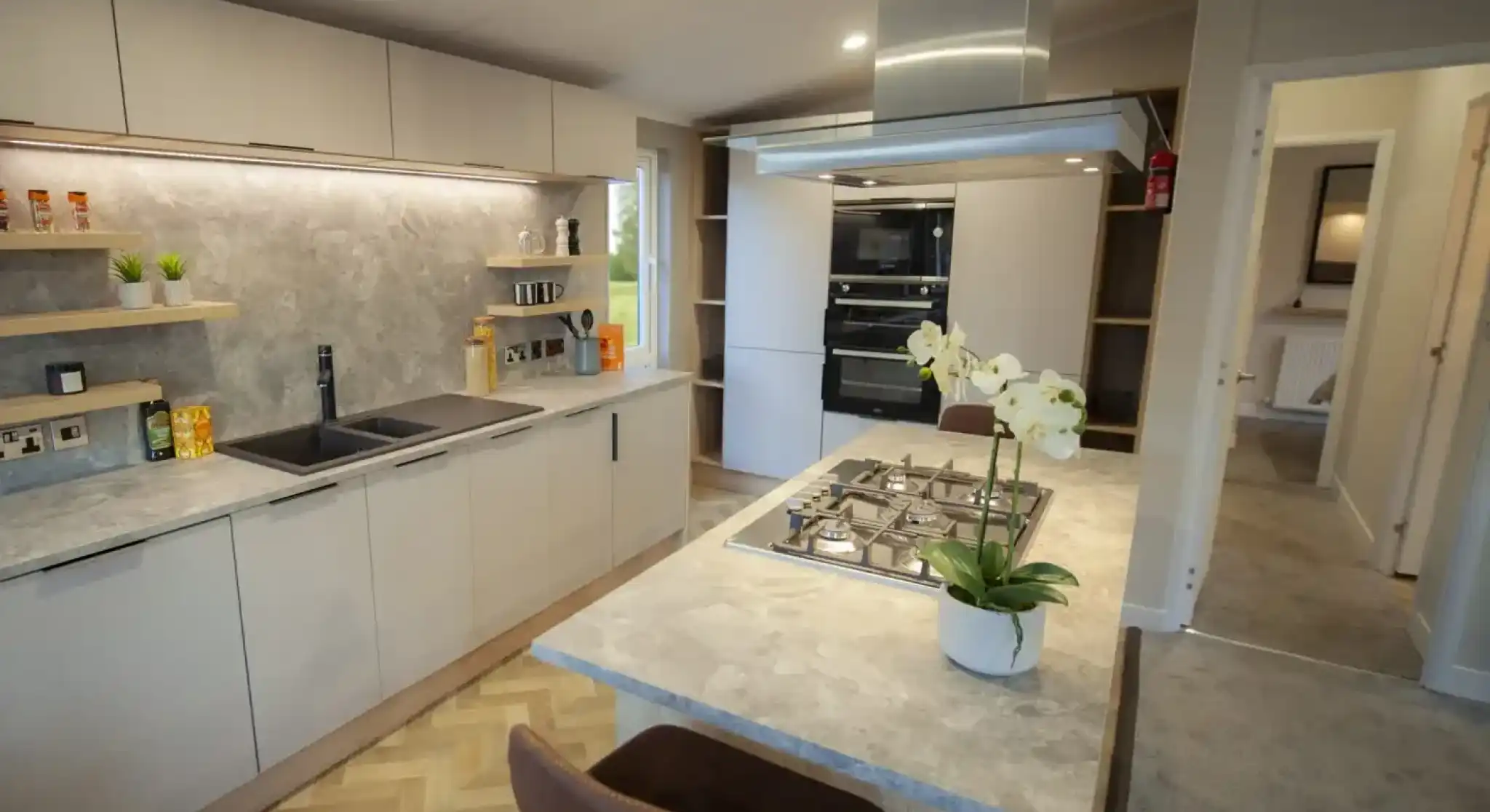 Modern kitchen featuring minimalist white cabinets, a marble countertop, and a built-in oven, illuminated by natural and recessed lighting.
