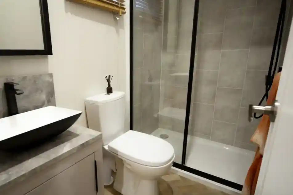 Modern bathroom with a black and white vessel sink, a white toilet, and a glass-enclosed shower with grey tiled walls.