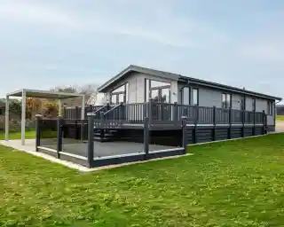 A modern gray house with a large deck and surrounding grass. A canopy structure is nearby, creating an outdoor seating area.