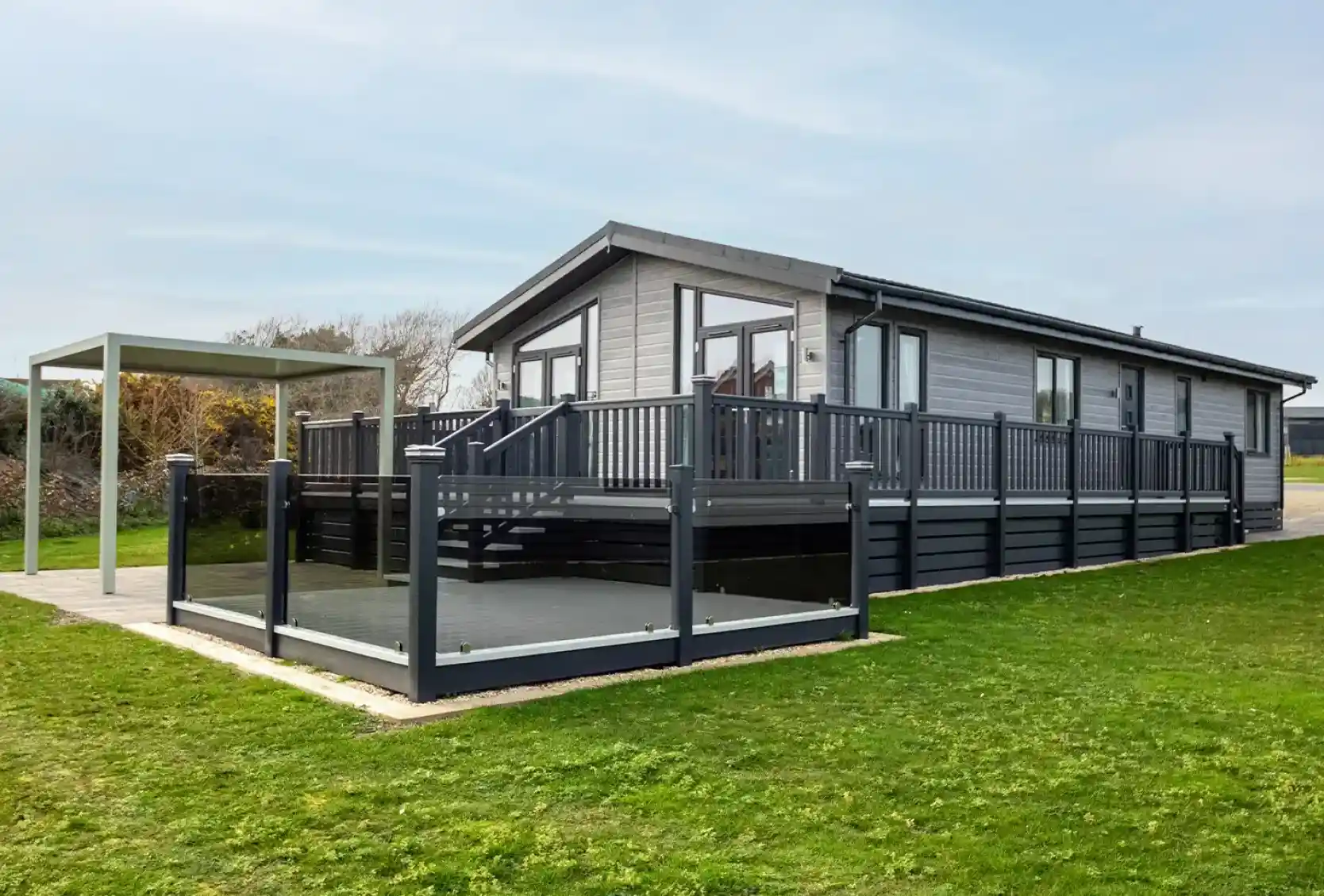A modern gray house with a large deck and surrounding grass. A canopy structure is nearby, creating an outdoor seating area.
