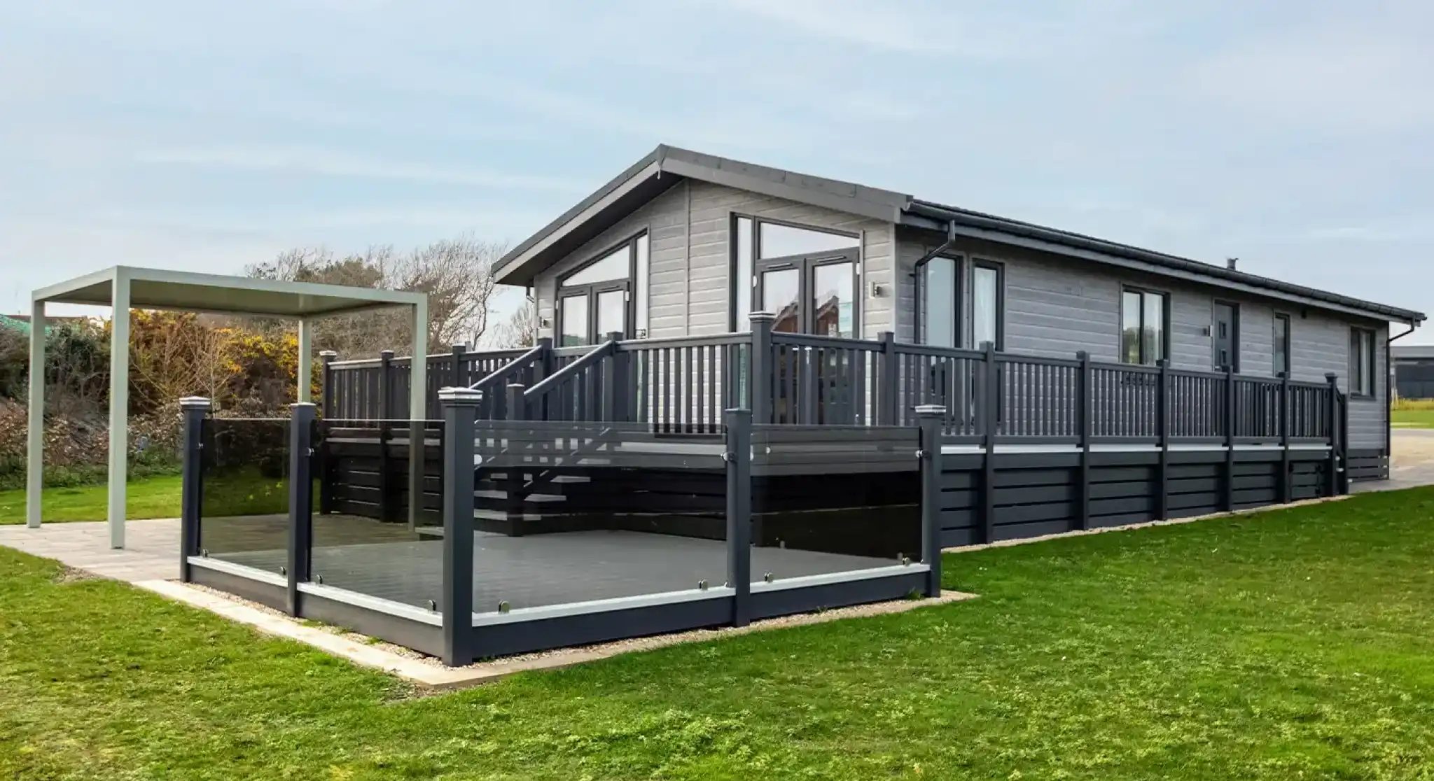 A modern gray house with a large deck and surrounding grass. A canopy structure is nearby, creating an outdoor seating area.