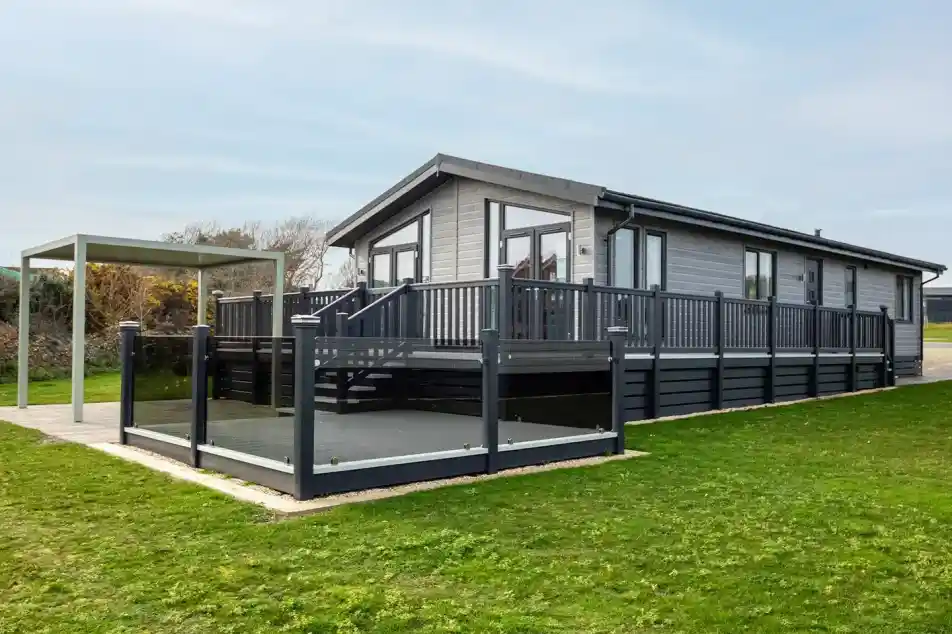 A modern gray house with a large deck and surrounding grass. A canopy structure is nearby, creating an outdoor seating area.