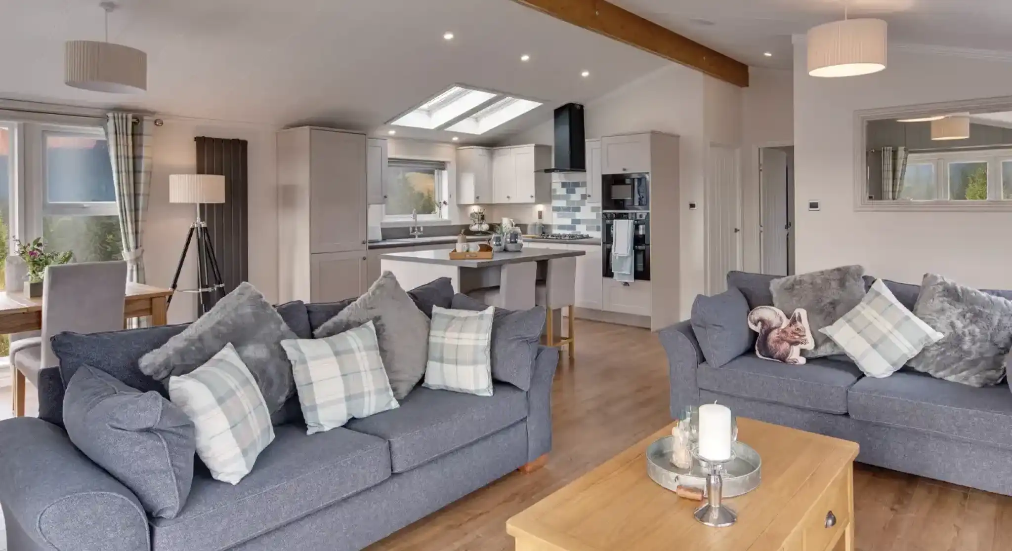 A spacious living room and kitchen area with two grey sofas, a wooden coffee table with a candle, and a modern kitchen island.