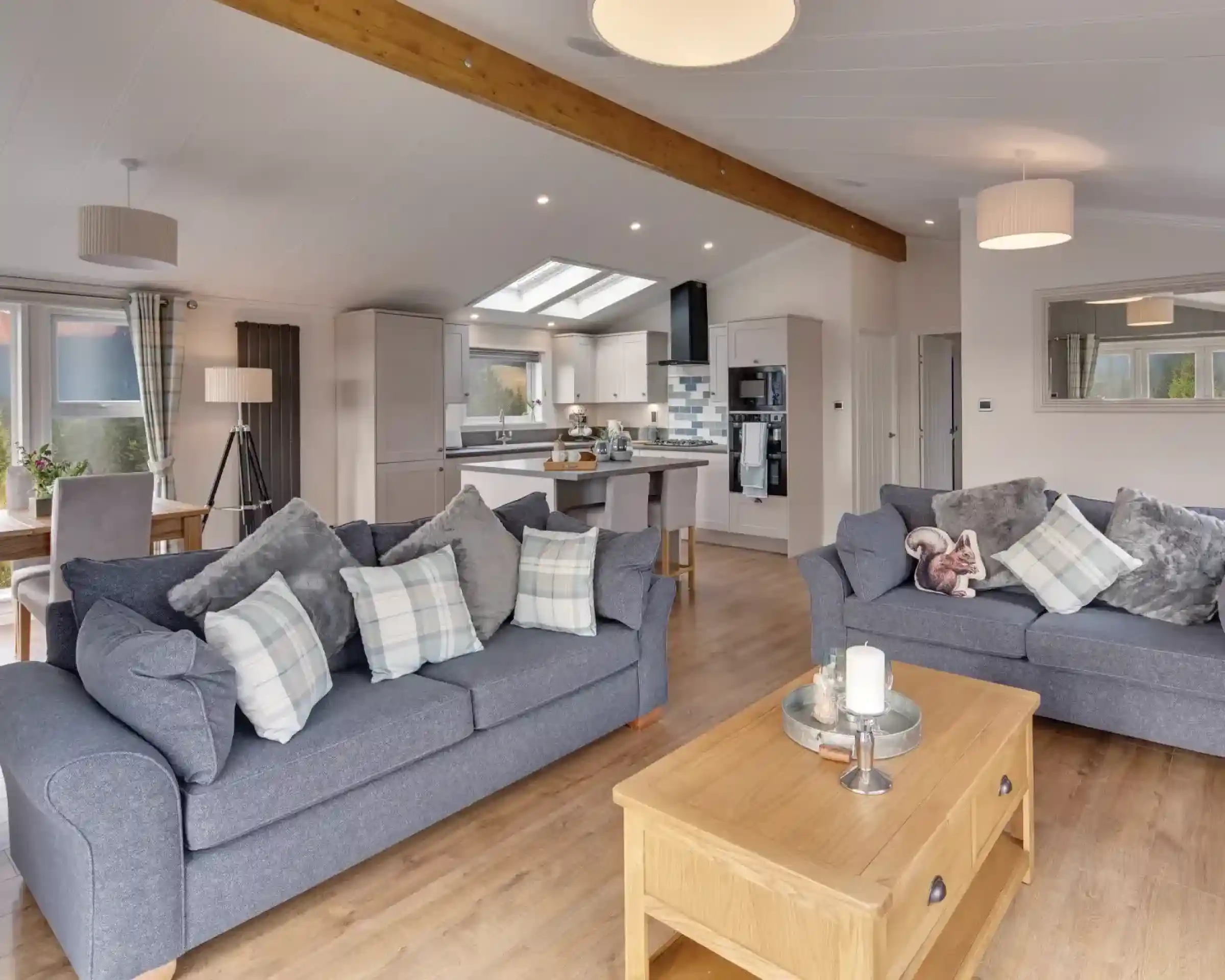 A spacious living room and kitchen area with two grey sofas, a wooden coffee table with a candle, and a modern kitchen island.