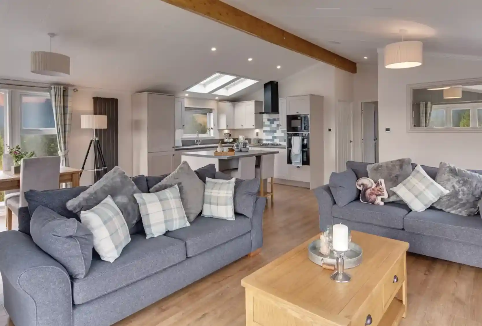 A spacious living room and kitchen area with two grey sofas, a wooden coffee table with a candle, and a modern kitchen island.