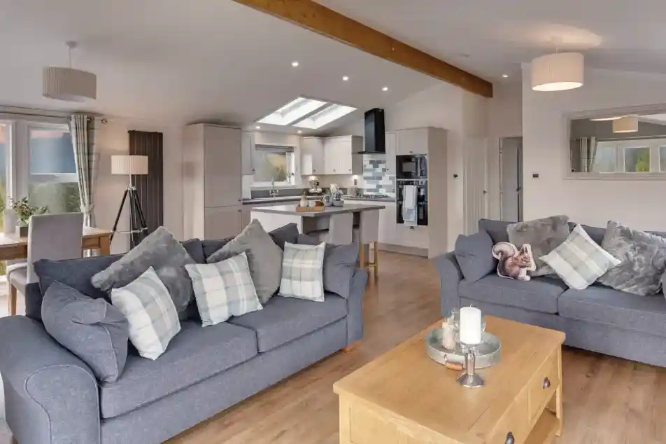 A spacious living room and kitchen area with two grey sofas, a wooden coffee table with a candle, and a modern kitchen island.