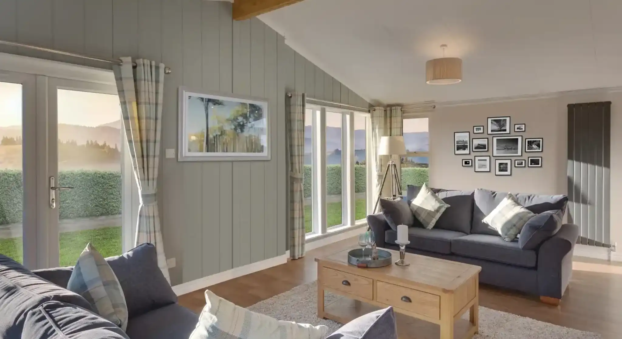 Spacious living room with vaulted ceiling, grey sofas, and large windows offering scenic views.