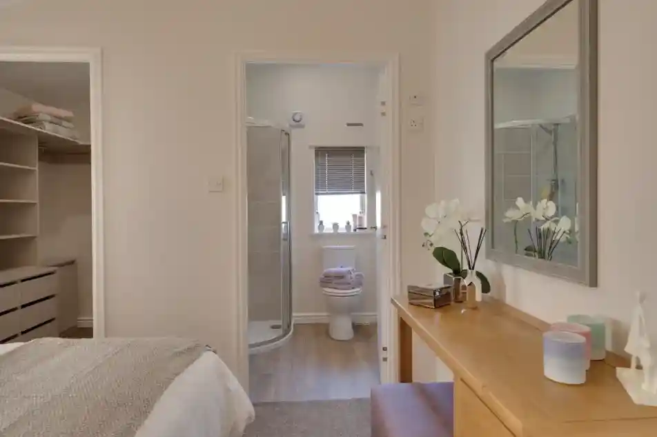 Bedroom with an open doorway to a bathroom with a toilet and shower, and a vanity with a mirror.