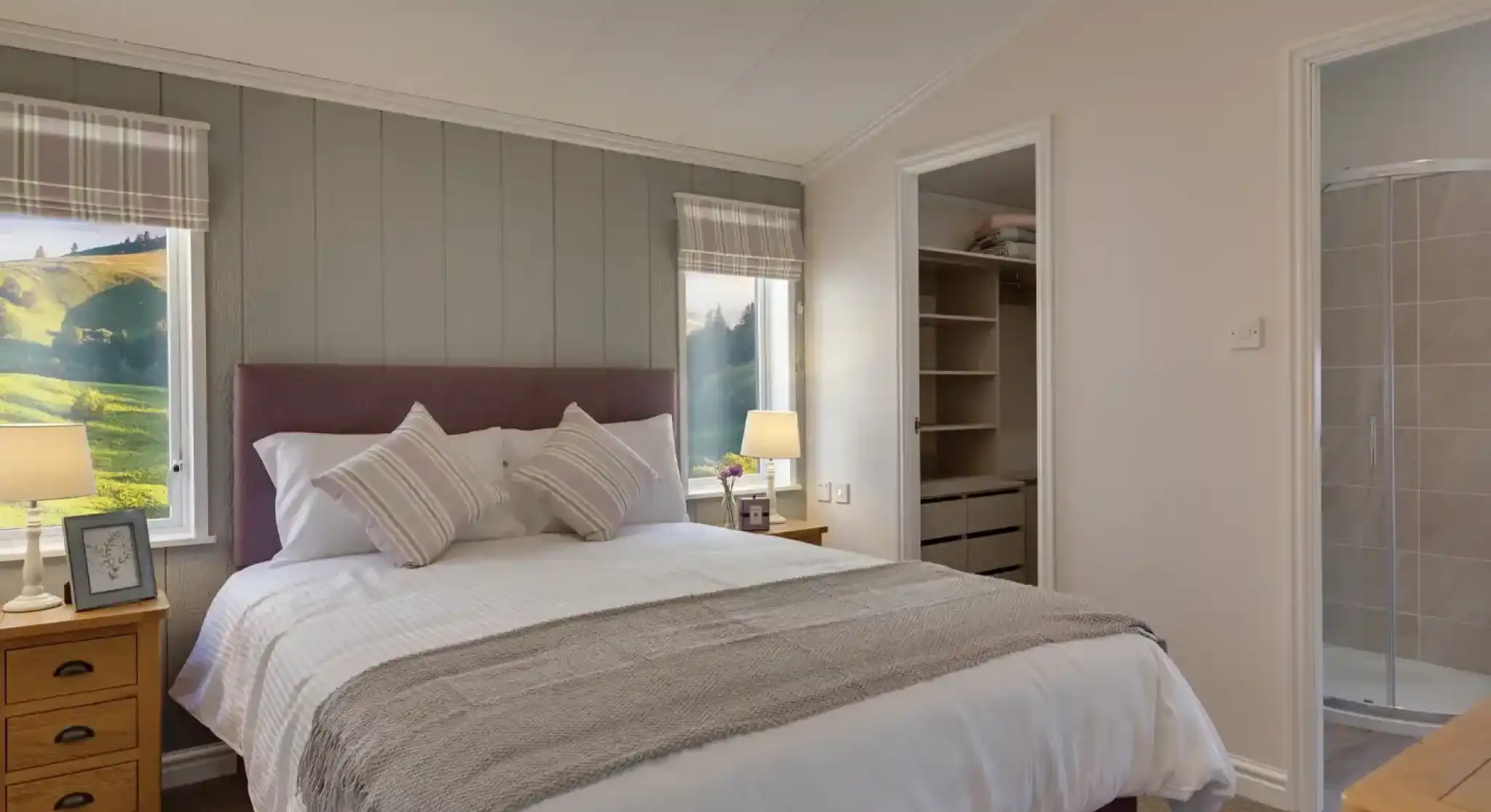 Spacious bedroom with a king-size bed, countryside views through plaid-curtained windows, and an open closet with a walk-in shower.