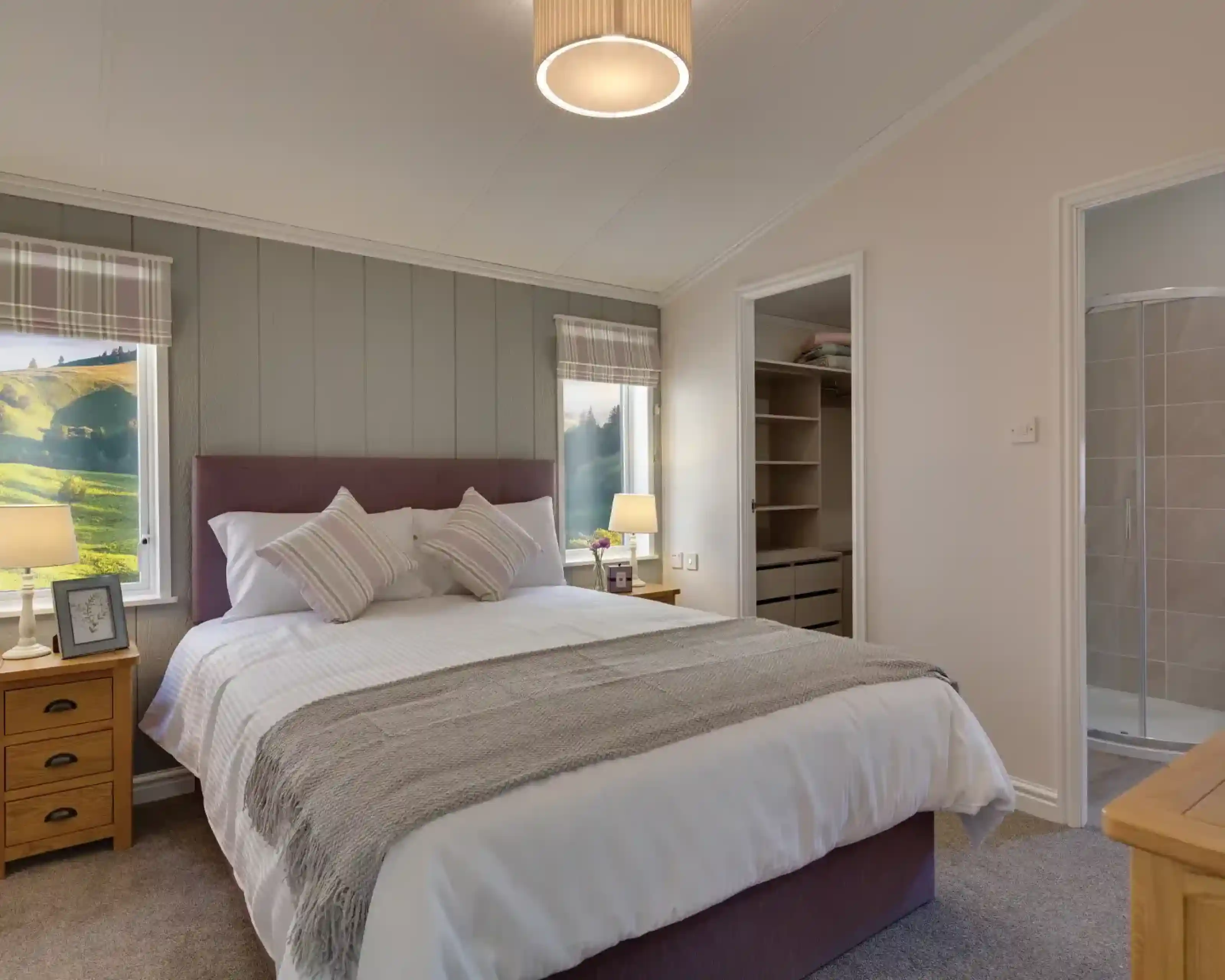 Spacious bedroom with a king-size bed, countryside views through plaid-curtained windows, and an open closet with a walk-in shower.