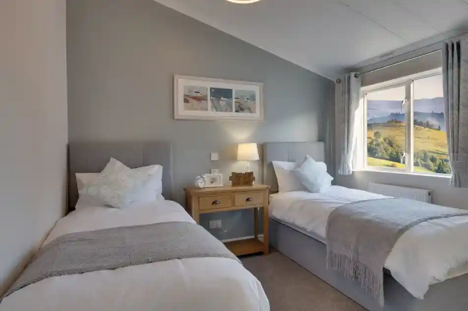 Two large single beds are positioned in a serene bedroom with a scenic view through the window.