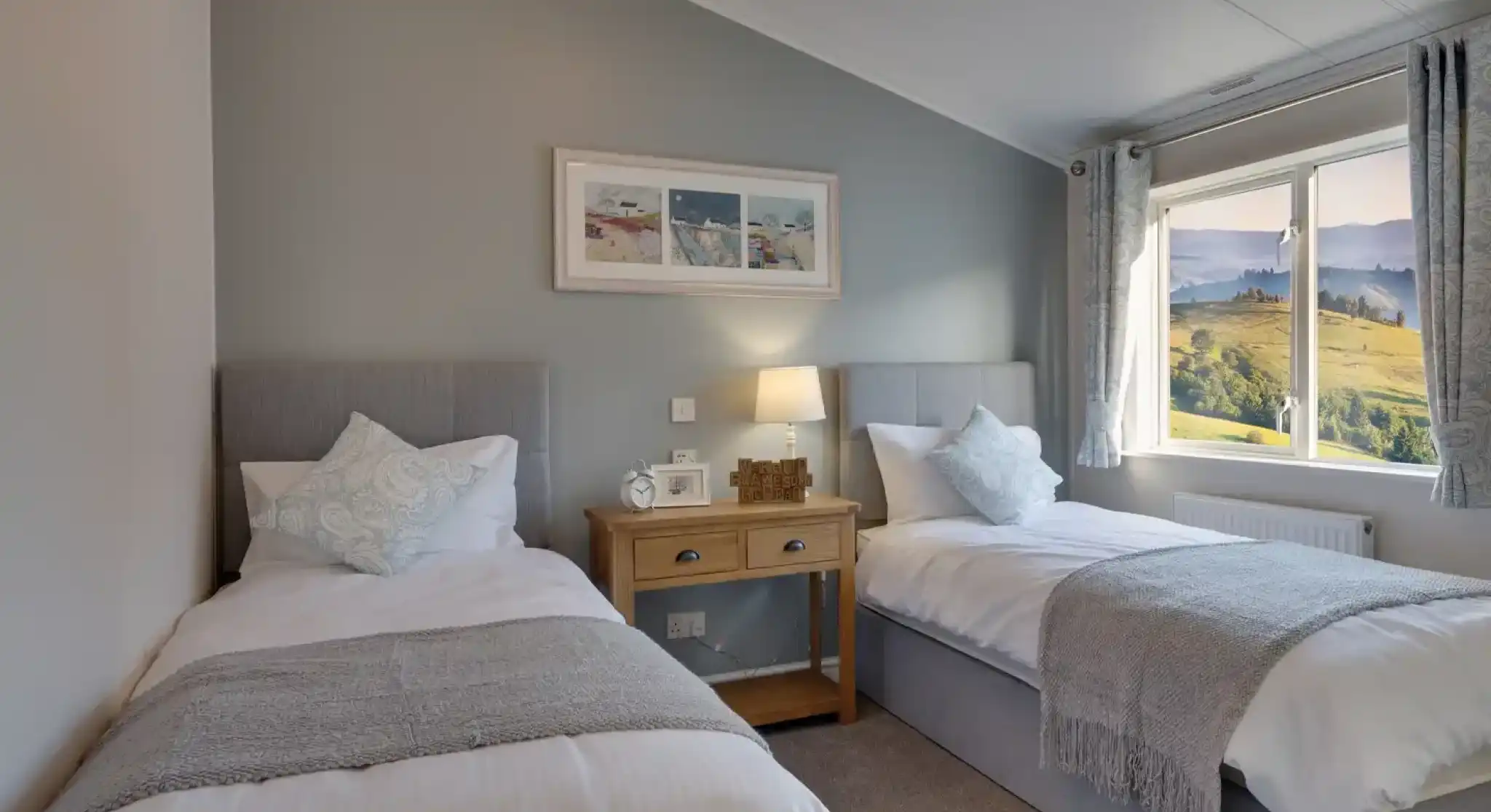 Two large single beds are positioned in a serene bedroom with a scenic view through the window.