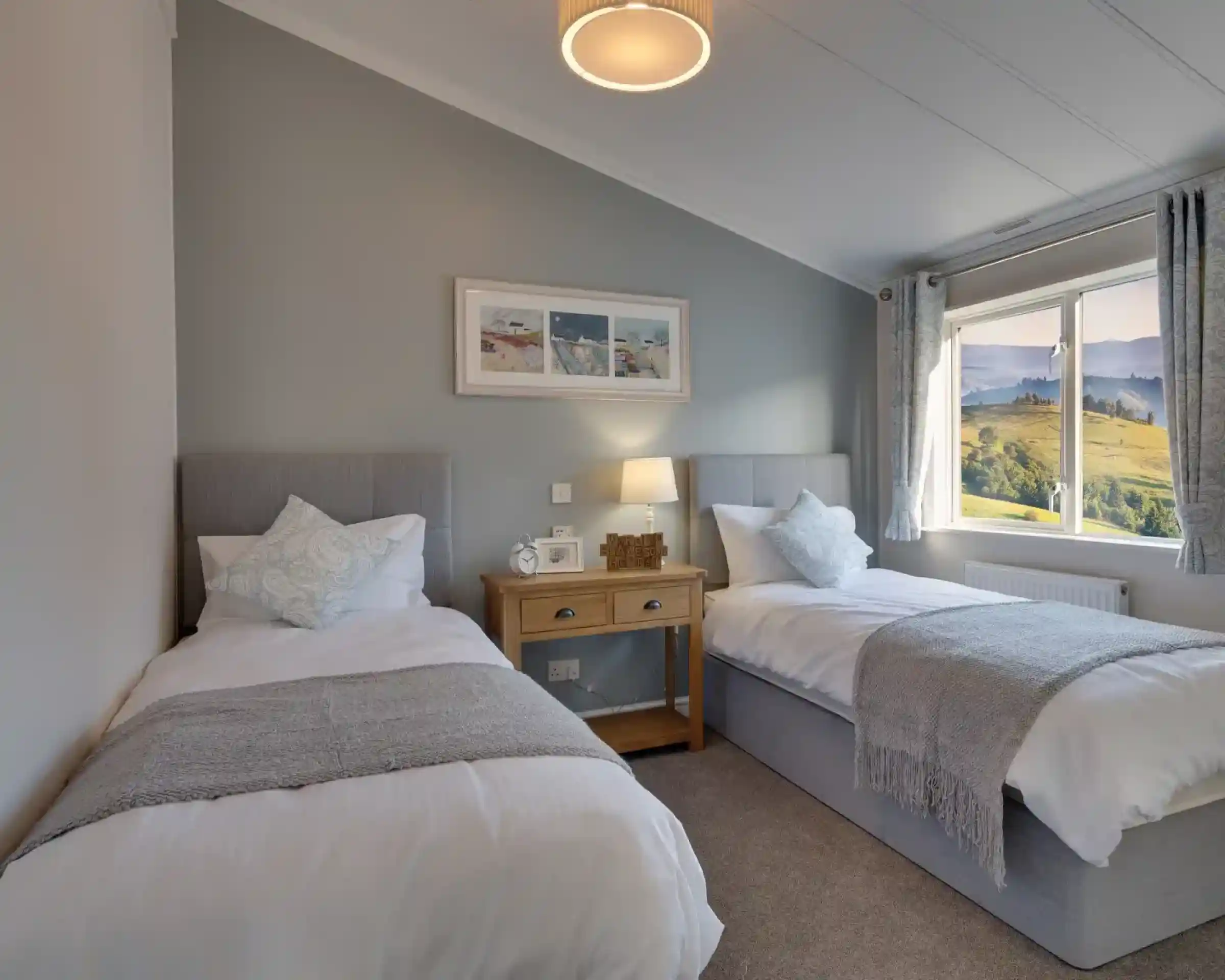 Two large single beds are positioned in a serene bedroom with a scenic view through the window.