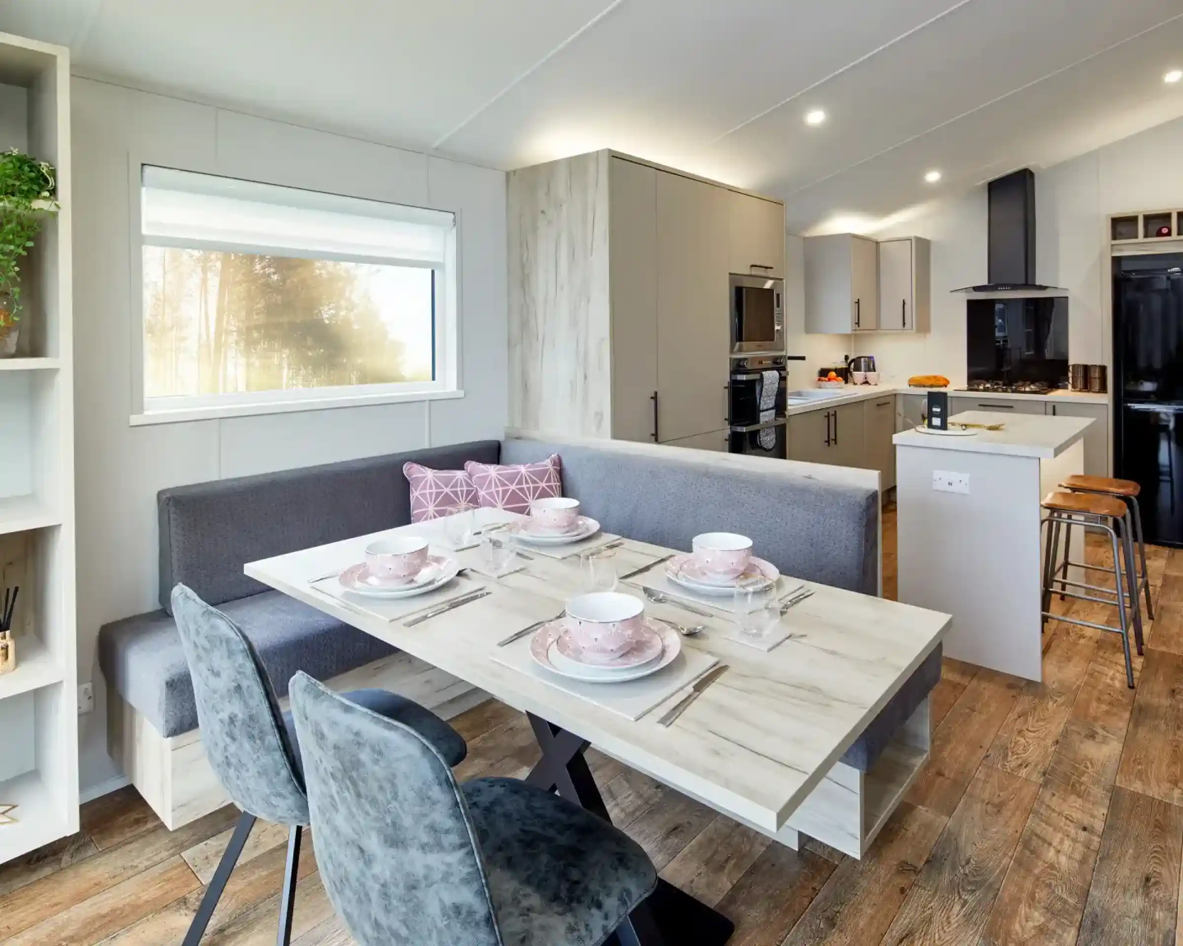Modern dining area with a U-shaped banquette, table set for four, and a contemporary kitchen in the background.