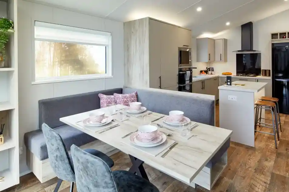 Modern dining area with a U-shaped banquette, table set for four, and a contemporary kitchen in the background.