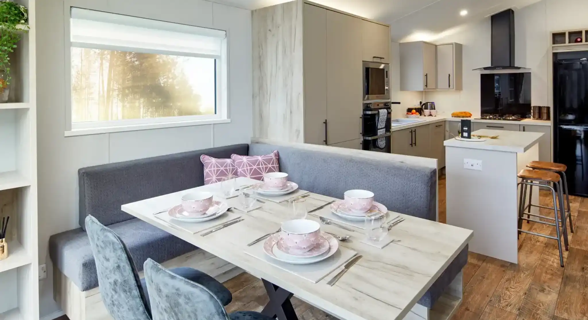 Modern dining area with a U-shaped banquette, table set for four, and a contemporary kitchen in the background.